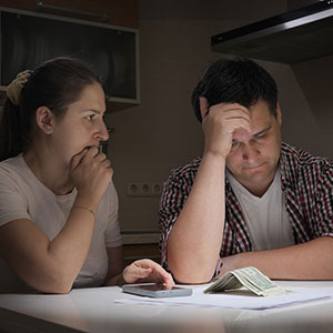 image of man and woman frustrated with hands on their head and bills and small amount of cash on table